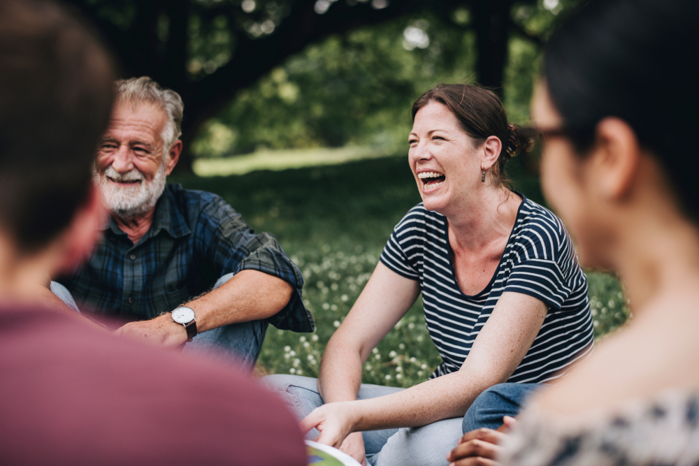 Old friends sit on the grass and laugh with each other.