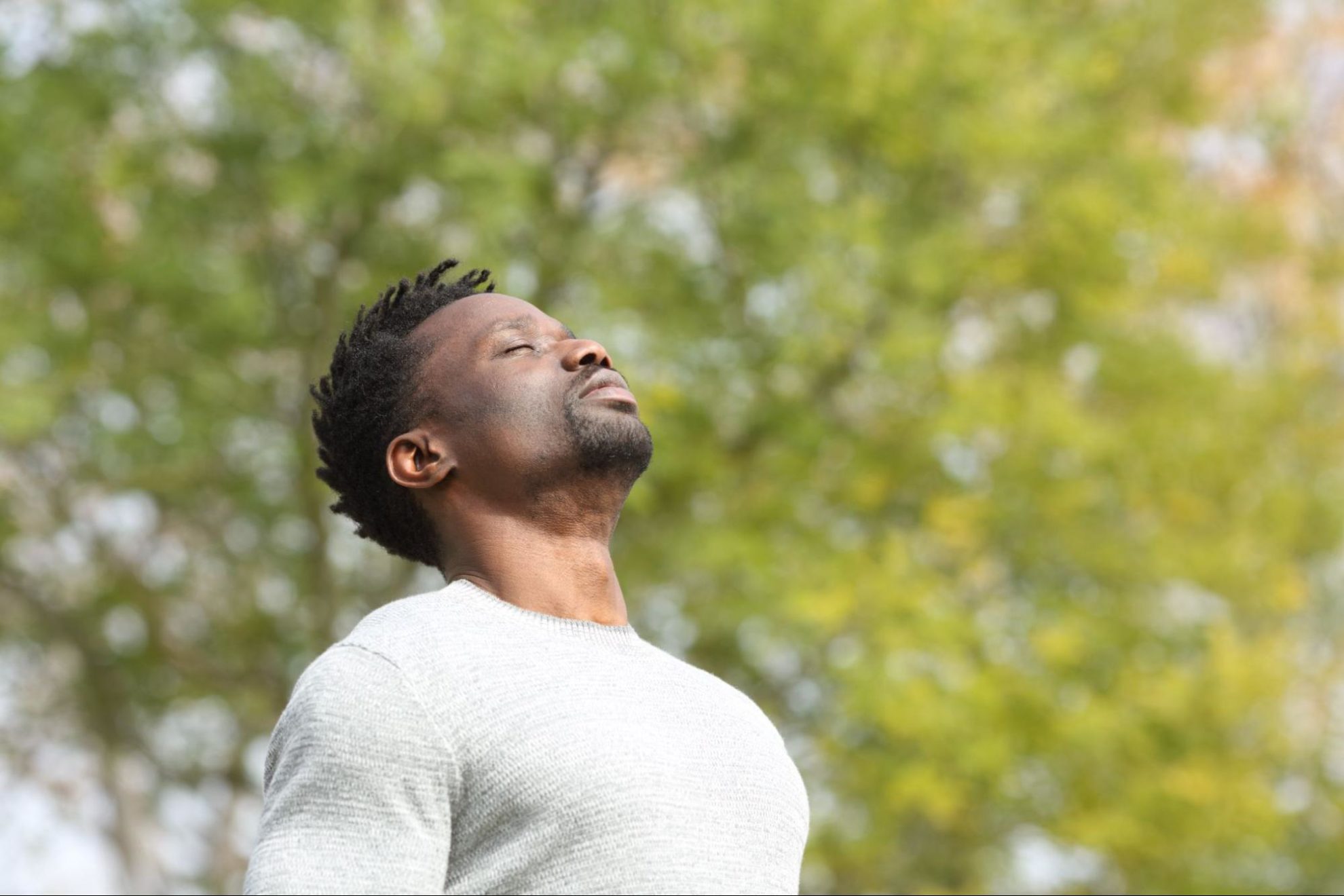 Black serious man breathing deeply fresh air in a park a sunny day with a green tree in the background